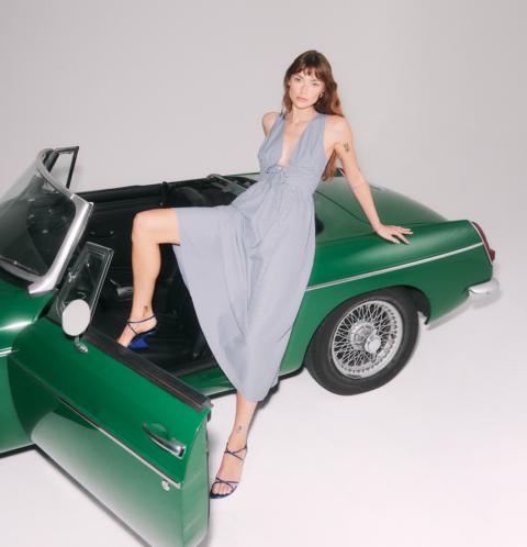 A model lays on a convertible in a long dress